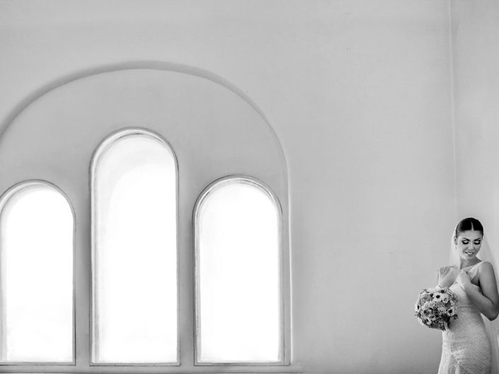 Mireasa cu buchet lângă ferestre arcuite albe, minimalist