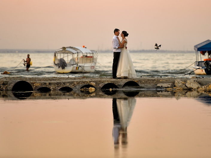 Mirii pe un ponton la mare, cu reflexie în apă și o barcă