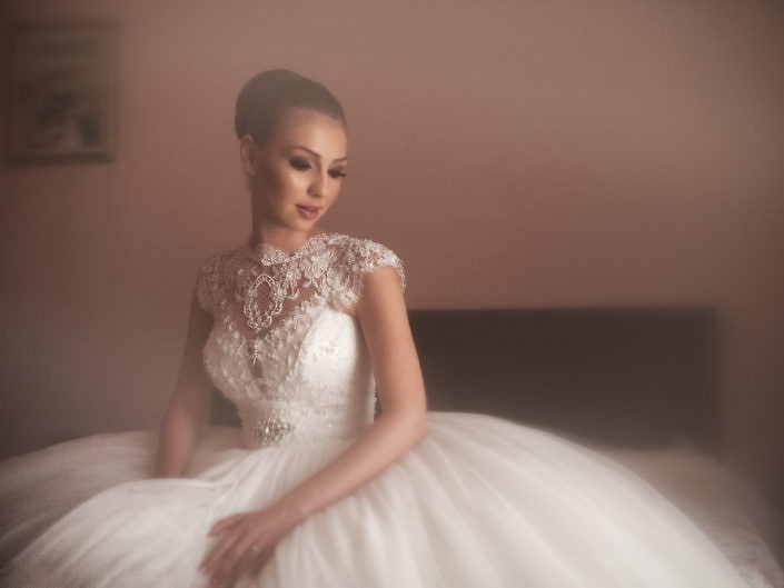 Mireasa așezată pe pat, în rochie amplă, portret în lumină de fereastră