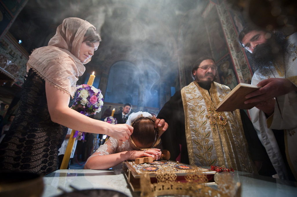 Mireasa cu basma și lumânare aprinsă la cununia religioasă, cu preoții citind în fumul de tămâie