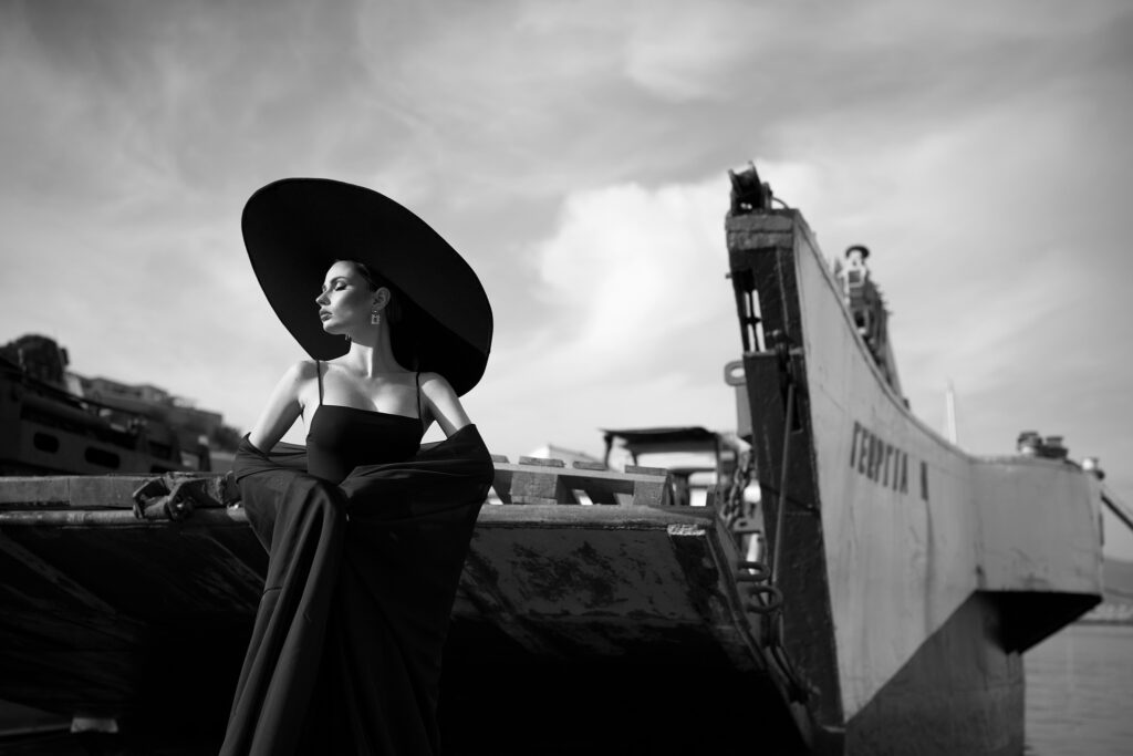 Ședință foto în Grecia: dark bride pe puntea unei bărci în portul Hydra, cu pălăria neagră