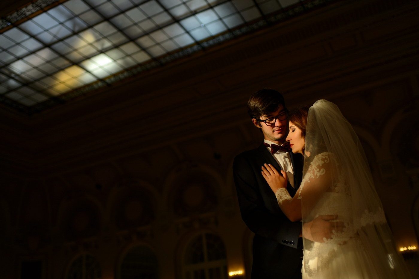 Fotografii de nuntă noaptea: mirii îmbrățișați într-o clădire istorică, luminați cald, cu plafonul de sticlă deasupra