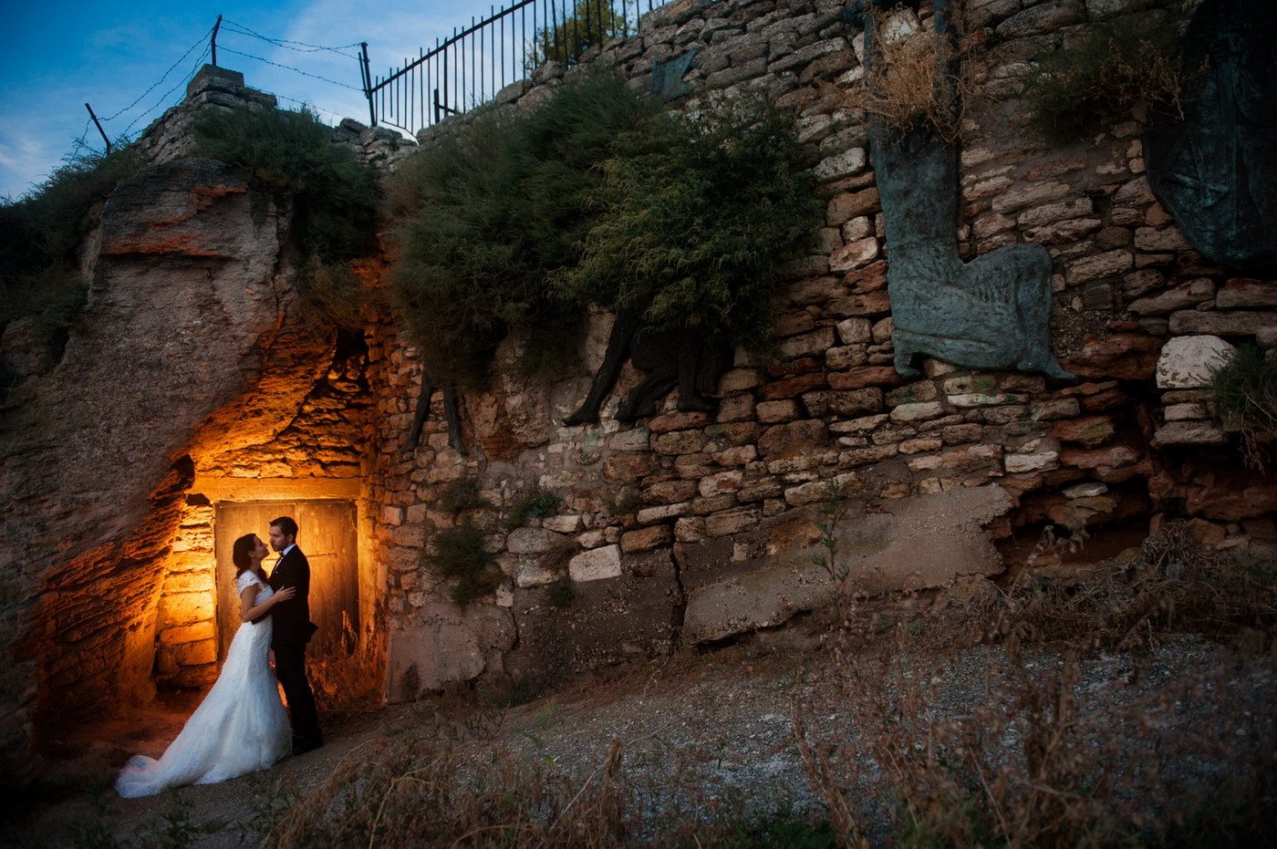 Mirii în pragul unei intrări din ruine de piatră, luminați cald din interior, noaptea