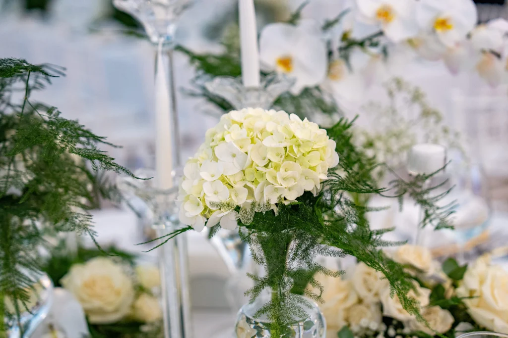 Aranjament floral cu hortensii, orhidee și trandafiri albi pe masa de nuntă