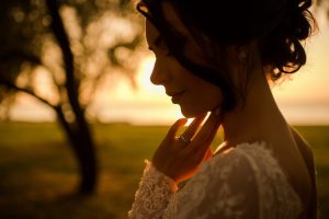 Portret de mireasă la apus: profilul miresei în contralumină aurie, cu mâna la bărbie și un copac în fundal