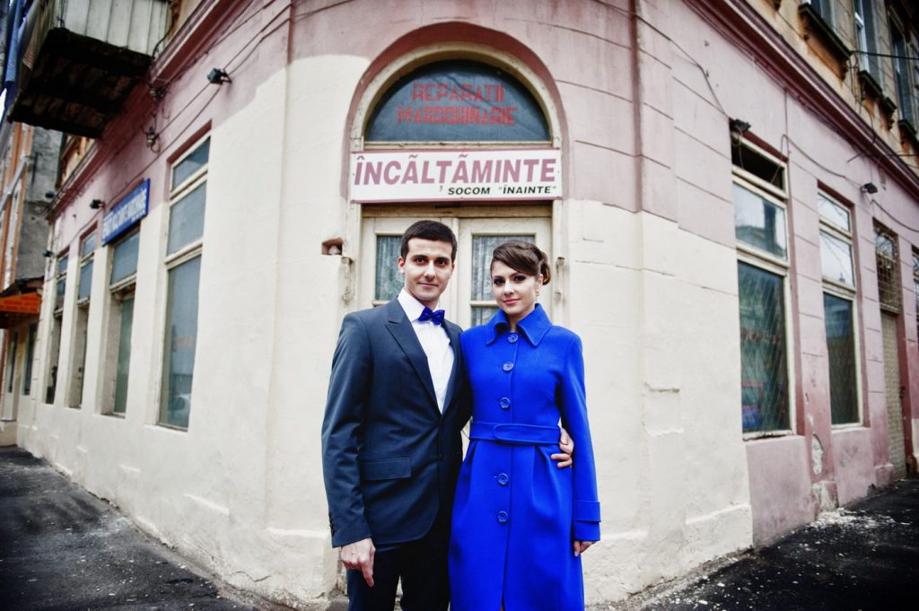 Cuplul în fața unei clădiri vechi, mireasa în palton albastru